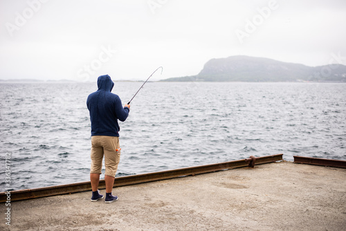Angler catching the fish during dull rainy stormy wheather. Mountains at background