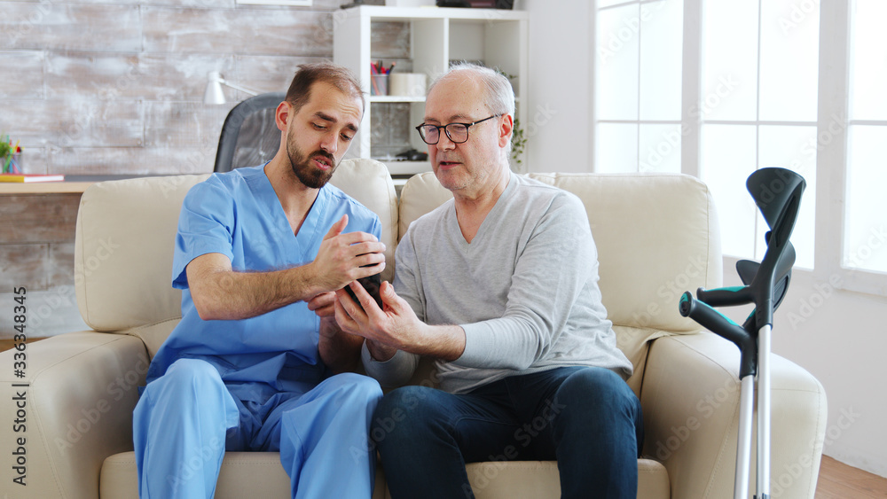 Male nurse helps a retired old man to use a smartphone Male nurse helps a retired old man to use a smartphone