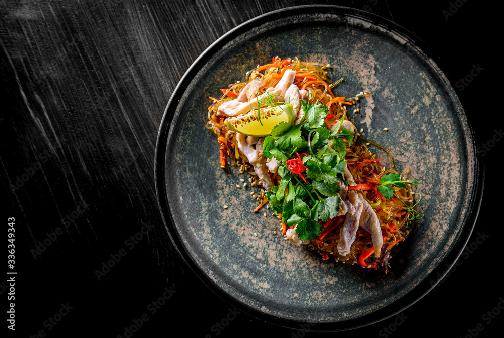 Udon stir-fry noodles with chicken meat, vegetables and sesame in plate on black wooden table background