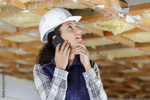 Fotografie female builder using smartphone to communicate problem with ceiling