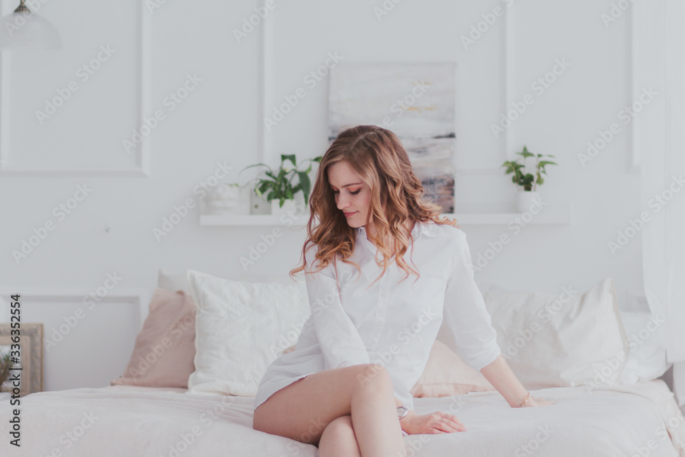 Young beautiful woman in white shirt sitting on bed and looking down. Young beautiful woman in white shirt sitting on bed and looking down.