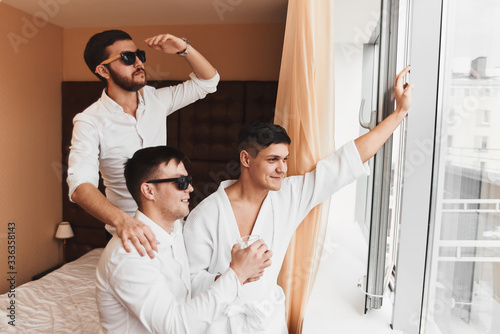 The groom is going to the wedding. Photosession of three energetic guys at the hotel. Brown tones.