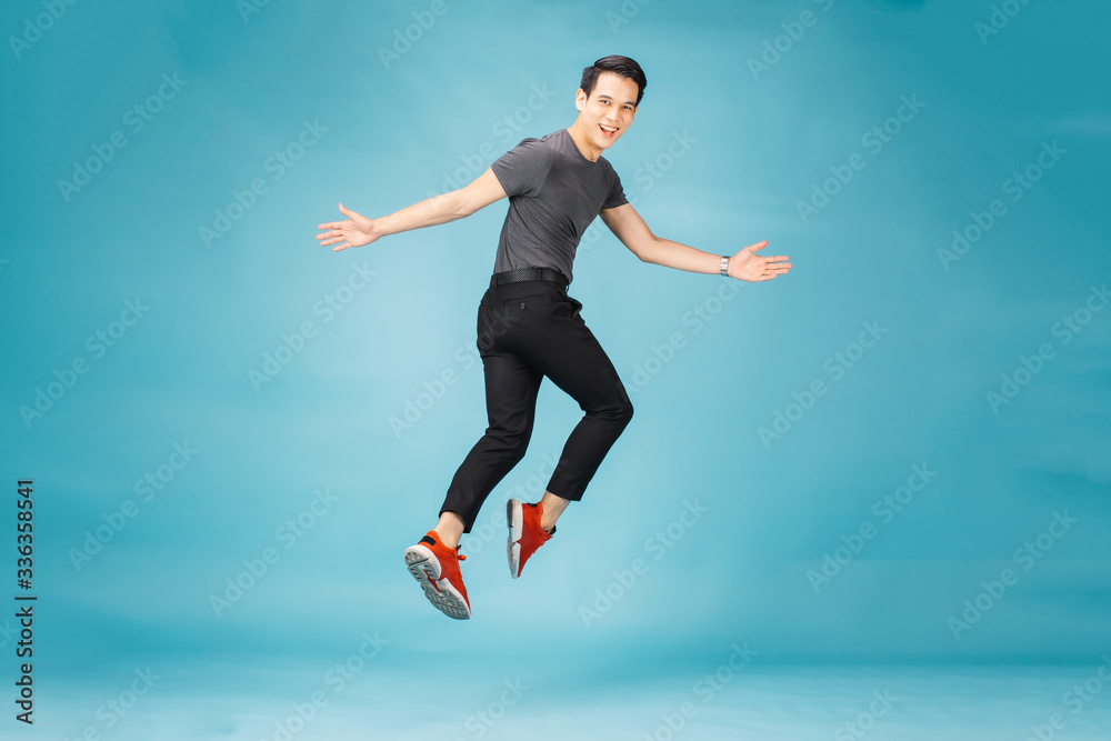 Hnadsome Asian man jumping isolated over blue wall background. 