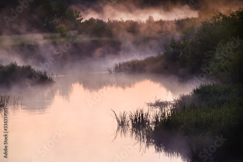 River in the early morning at dawn. Delicate dawn sky and fog rising above the water  lush greenery on the banks. Summer spring wild landscape by the river. Selective soft focus.