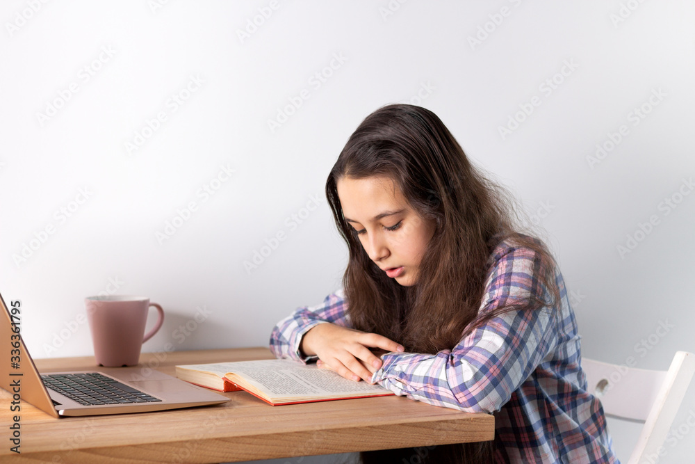 Distance learning at home.Teen girl with laptop does homework, reads a book, search information on the Internet. Elearning concept. Distance learning at home.Teen girl with laptop does homework, reads a book, search information on the Internet. Elearning concept.