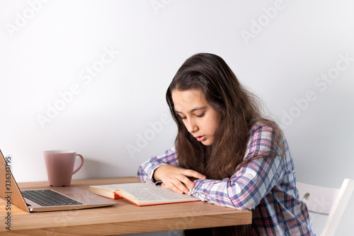 Distance learning at home.Teen girl with laptop does homework, reads a book, search information on the Internet. Elearning concept.