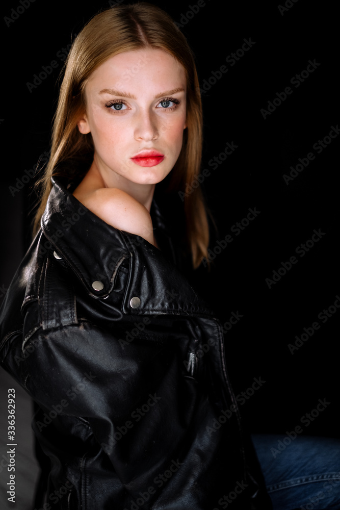 Portrait of a model girl in a black biker leather jacket. young woman with brown hair posing on black background