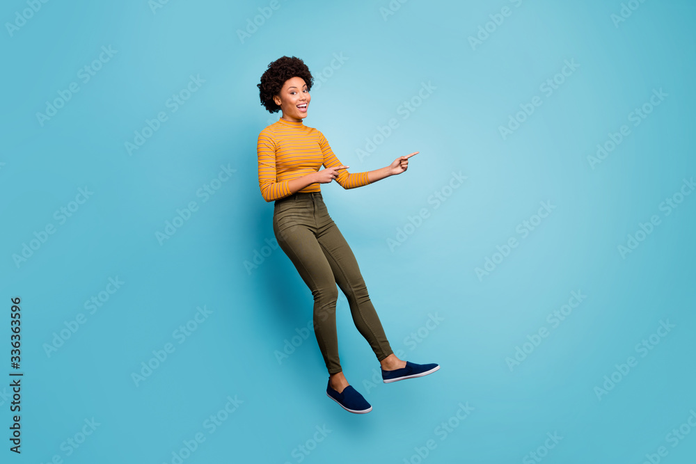 Full size photo of positive dark skin girl jump help choose decide advise feedback point index finger copyspace wear yellow striped sweater green pants trousers isolated blue color background Full size photo of positive dark skin girl jump help choose decide advise feedback point index finger copyspace wear yellow striped sweater green pants trousers isolated blue color background