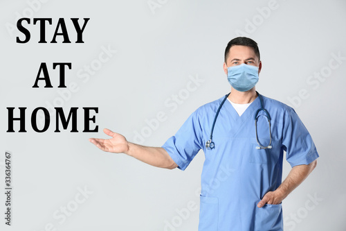 Doctor in medical mask and text STAY AT HOME on light background