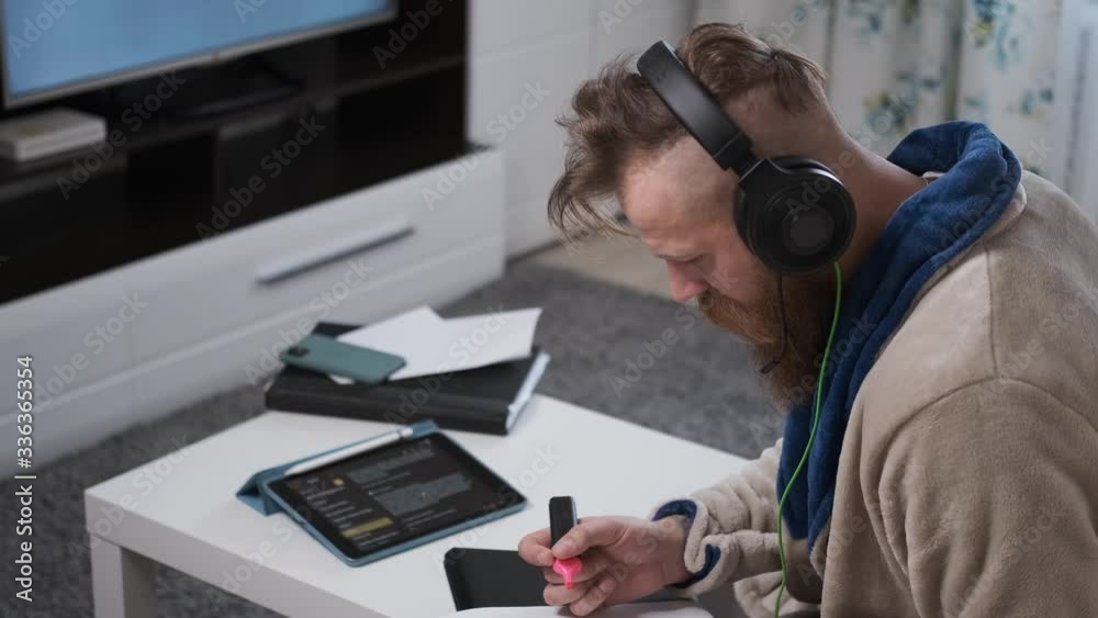 man with beard and mustache works at home in large headphones with laptop and draws with marker, watching news,in quarantine of global coronavirus epidemic man with beard and mustache works at home in large headphones with laptop and draws with marker, watching news,in quarantine of global coronavirus epidemic