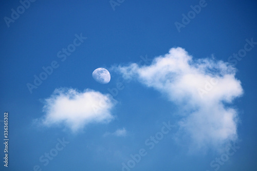 Rising moon with white clouds on a background of blue sky. Photo taken in April 2020.