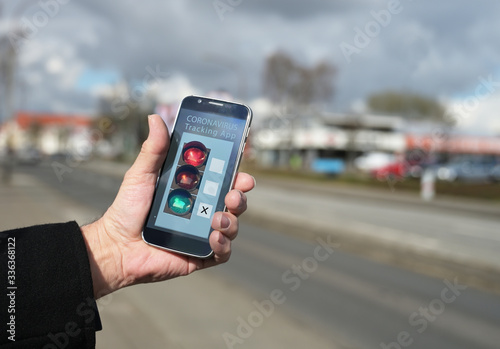 Older male hand is holding a smartphone with a coronavirus tracking app, which monitors contacts between people and shows the risk of infection, blurry city street background, copy space