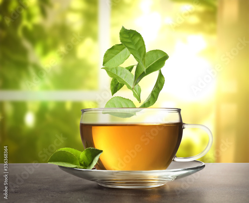 Green leaves falling into cup of tea on table against blurred background
