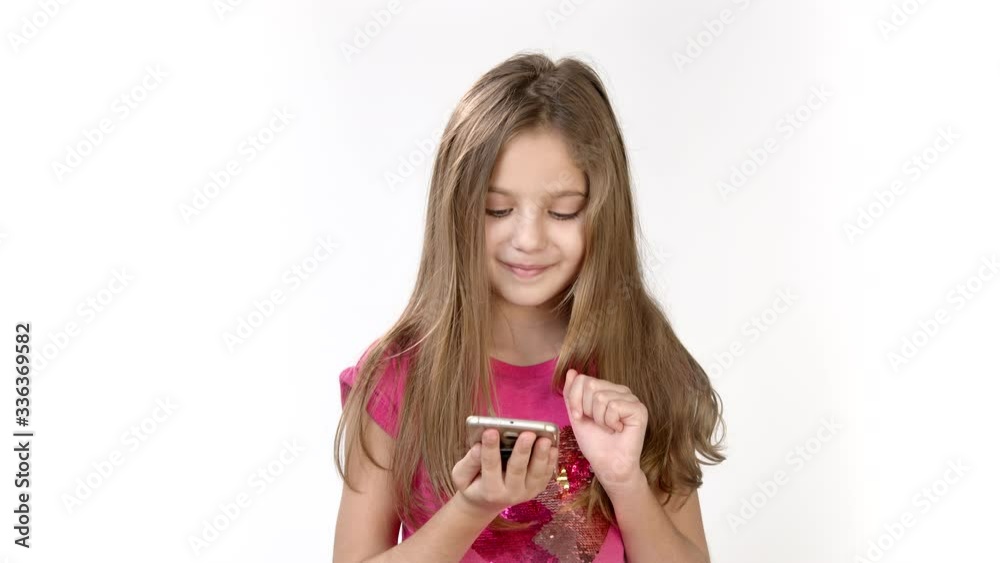 A little girl holds a mobile phone in her hand and taps the screen with her fingers. The girl works and plays on her mobile phone. A little girl holds a mobile phone in her hand and taps the screen with her fingers. The girl works and plays on her mobile phone.