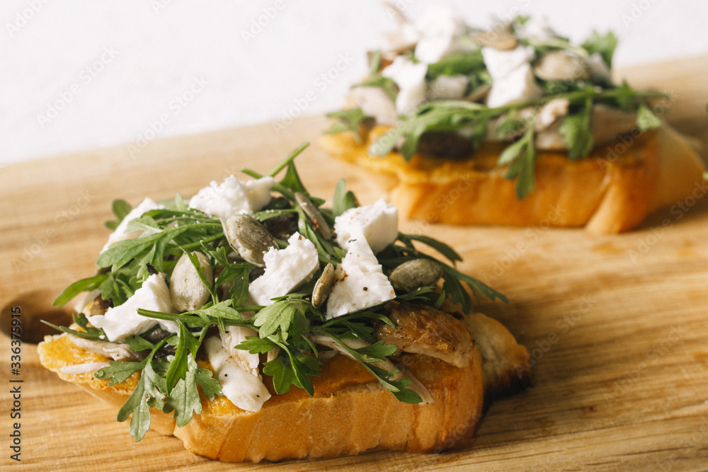 Italian appetizer - bruschetta with with arugula, parsley or cilantro, cheese and chicken on a wooden board Italian appetizer - bruschetta with with arugula, parsley or cilantro, cheese and chicken on a wooden board