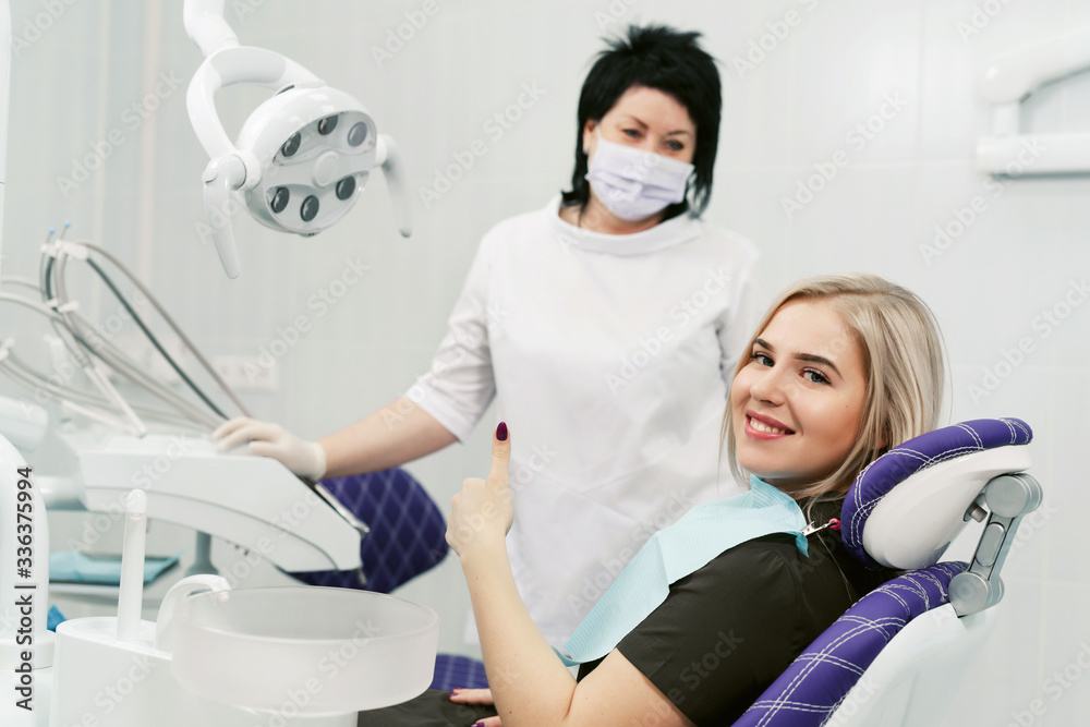 Smiling female patient looking at camera at dental clinic. Doctor with facial disposable medical mask Smiling female patient looking at camera at dental clinic. Doctor with facial disposable medical mask