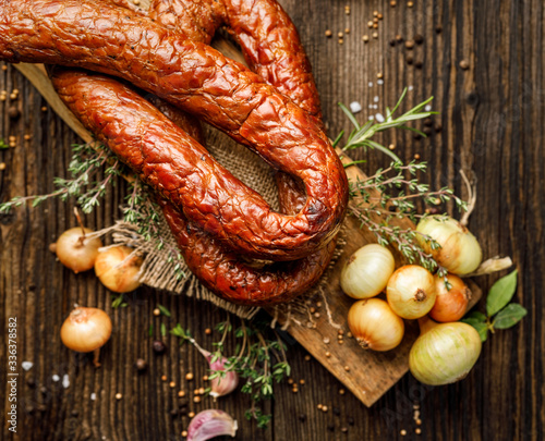 Smoked sausage on a wooden rustic table with addition of fresh aromatic herbs and spices, top view. Natural product from organic farm, produced by traditional methods