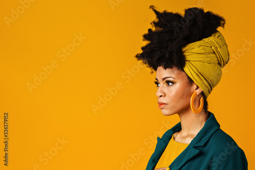 Profile portrait of a serious young woman with big yellow earrings and afro hair wrapped with head wrap scarf photo