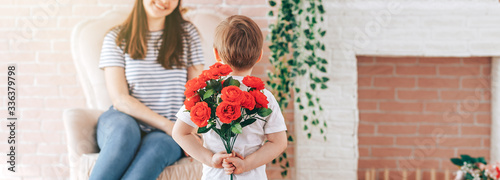 Boy holding a bouquet of flowers behind his back, the son gives his mother flowers, what to present to his mother for his birthday, March 8, mother's day