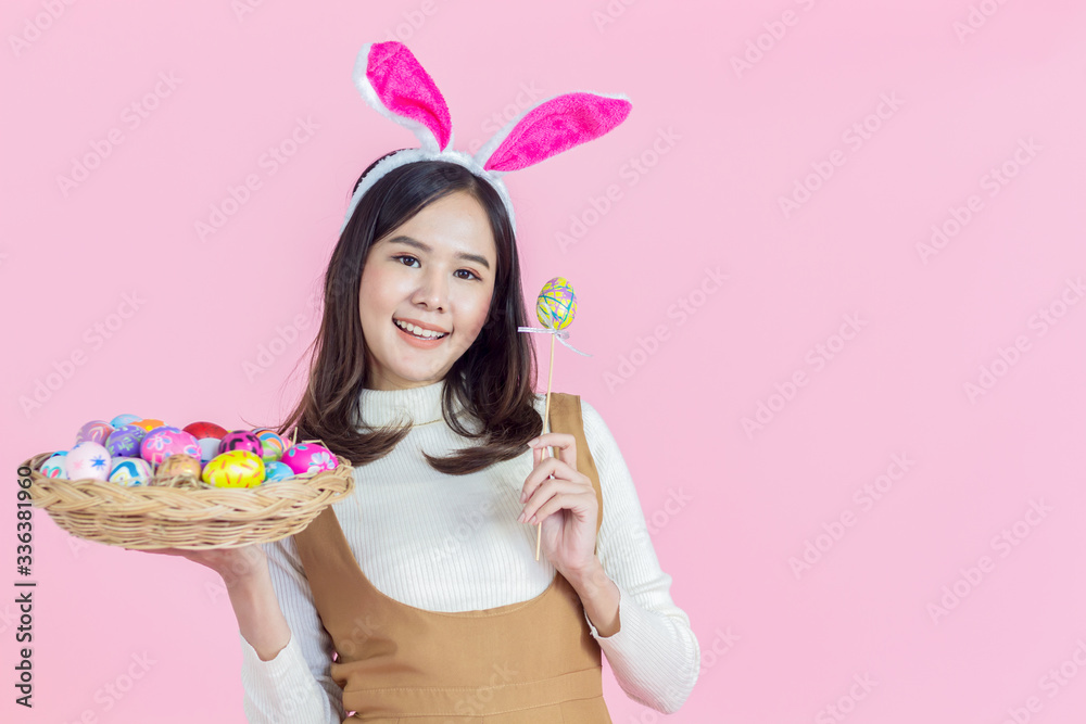 Asian young woman wearing bunny holding a colorful egg basket for Easter on a pink background. girl smiled happily copy space. Asian young woman wearing bunny holding a colorful egg basket for Easter on a pink background. girl smiled happily copy space.