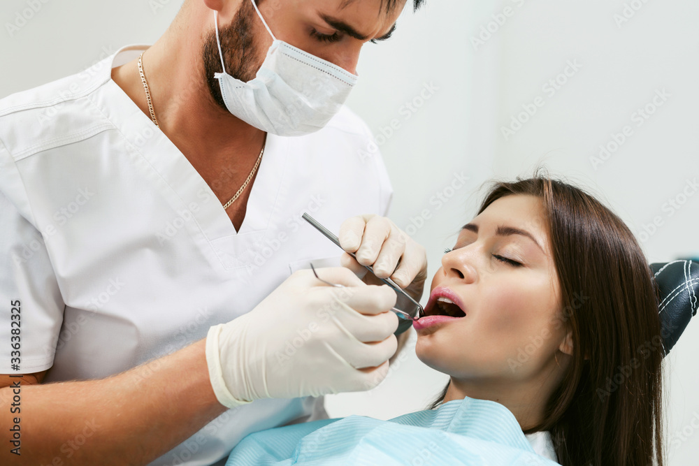 Dentist examining a patient's teeth in modern dentistry office. Closeup cropped picture with copyspace. Doctor in disposable medical facial mask. Dentist examining a patient's teeth in modern dentistry office. Closeup cropped picture with copyspace. Doctor in disposable medical facial mask.