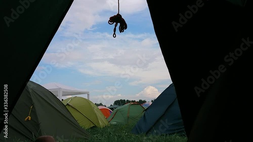 Inside view of the tent on a colorful tent city at a music festival. In the morning, sky, clouds, summer, spring, sun, day, wind, grass, legs, sneakers. Man lies photo