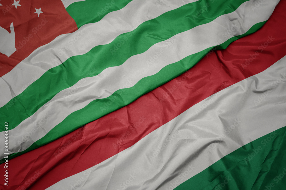 waving colorful flag of hungary and national flag of abkhazia.