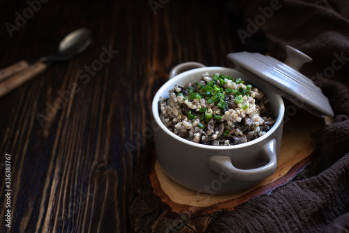 Buckwheat with mushrooms and green onions. A traditional Eastern European side dish or porridge. Healthy vegetarian dish. Served in a ceramic pan on a wooden table. Close-up