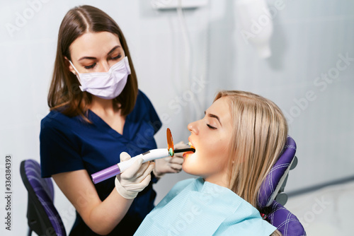 Dentist in facial medical mask working with dental polymerization lamp in oral cavity