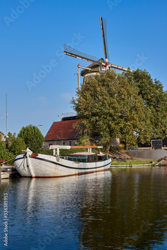Image of Dutch Sailing Tjalk on the canal in Amsterdam with a background of trees and a windmill. Netherlands, Holland photo