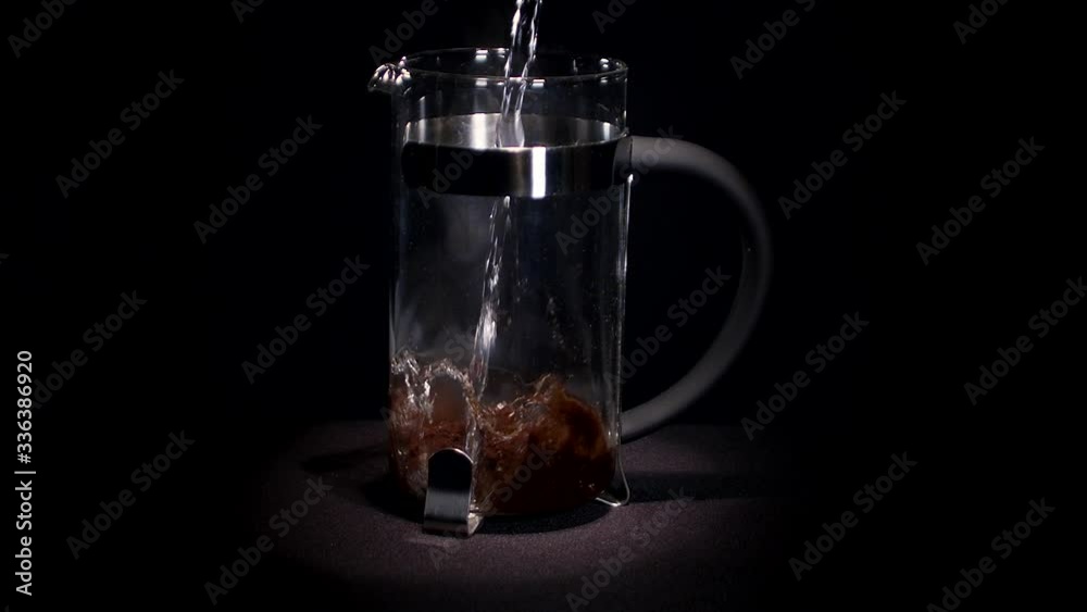 A wide shot of water being poured over ground coffee inside a french press coffee maker. A wide shot of water being poured over ground coffee inside a french press coffee maker.