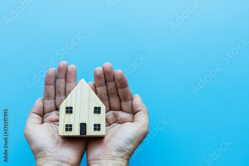Hand holding wooden house model on blue background for self-quarantine and staying home in coronavirus or Covid-2019 situation concept