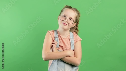 Thoughtful schoolgirl in glasses trying to make a decision with her arms crossed over her chest while standing on isolated background in the studio photo