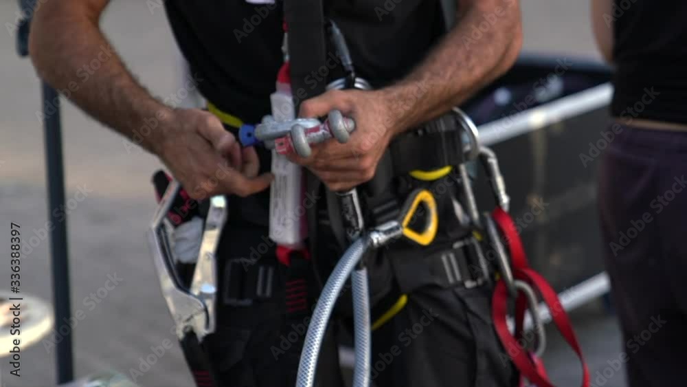 A climber attaches carious safety ropes, hooks and various climbing safety equipment using carabiners to his harness before he ascends the scaffolding to carry out his work
