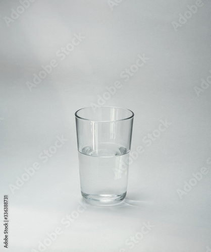 A glass cup half full of water stands on a light background. Close-up. Copy space