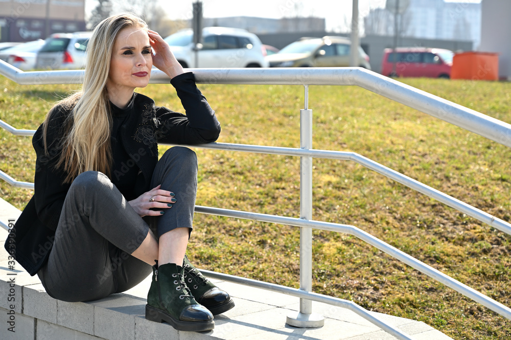 Model on the background of the railing of the stairs posing with a smile. Portrait of a young blonde Caucasian woman in the city outdoors on a sunny day.
