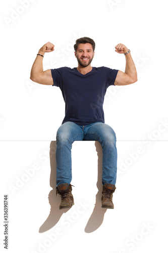 Happy Handsome Man Is Sitting On A Top And Flexing Muscles