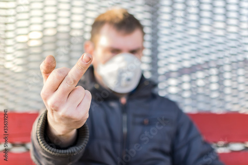 An impolite man in a medical mask shows an obscene and bad gesture with the middle finger to 