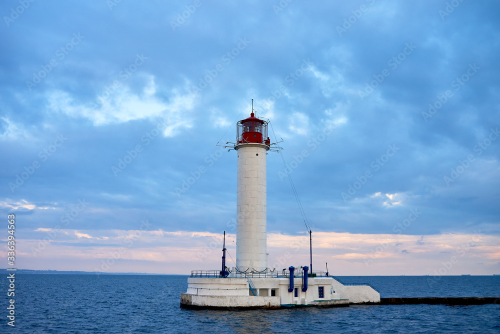 Red and white lighthouse in sea at sunset, copy space. Summer seascape with light house. Black sea