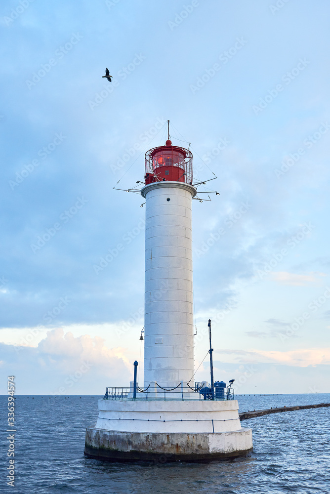 Red and white lighthouse in sea at sunset, copy space. Summer seascape with light house. Black sea