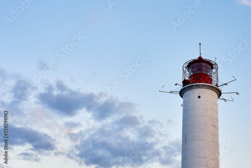 Red and white lighthouse at sunset against blu sky background  copy space. Summer seascape with light house