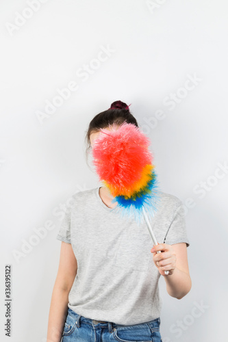 Girl holds brush to clean dust and closes her face on grey background photo