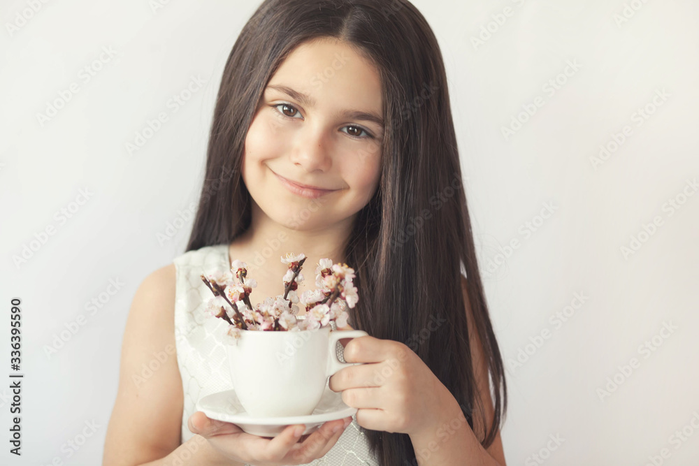 Spring consept. Happy cute child girl with blooming cherry flowers on twigs in a cup in the hands of a young girl indoors.