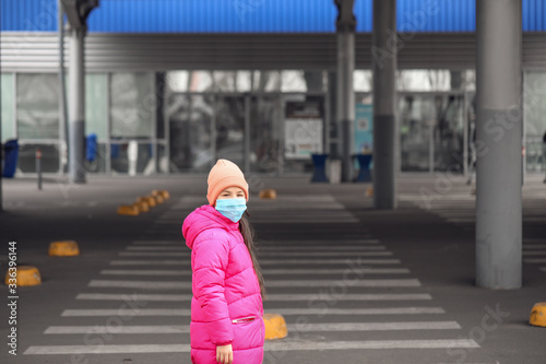 Little Asian girl wearing protective mask on city street. Concept of epidemic