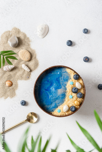 Smoothie bowl with blue spirulina decorated as a beach with fresh blueberries on gray stone background. Top view. Healthy nutrition, superfoods, dieting