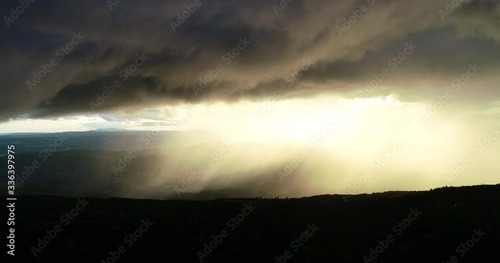 Aerial view of epic dramatic storm and rain over idyllic beautiful valley and mountains during sunset.