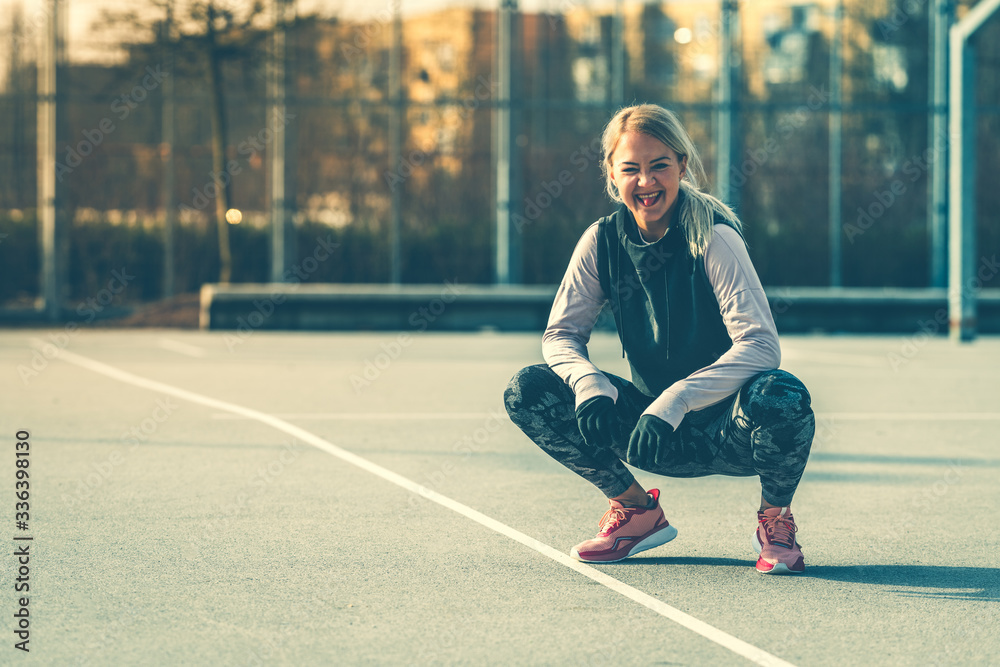 Smiling young Caucasian woman taking a exercises break, squatting and winking