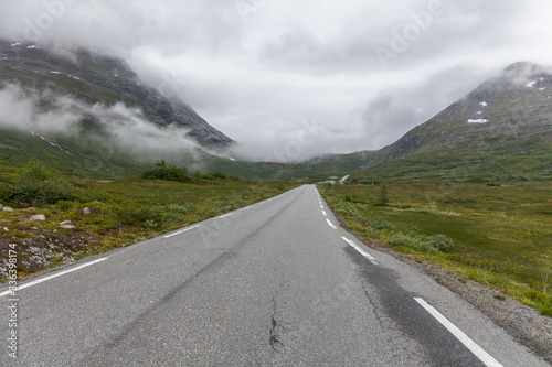 The road leading a mysterious gorge surrounded by clouds of the Norwegian mountains, selective focus