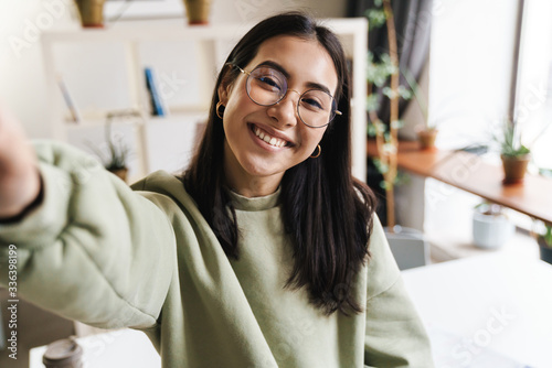 Cheery optimistic young girl student indoors take a selfie photo