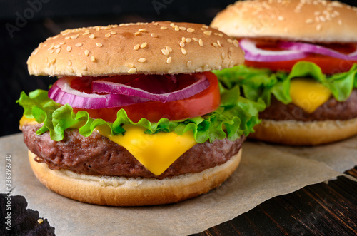 Two burgers on a wooden background. Beef burger with fresh lettuce, tomato and cheese.